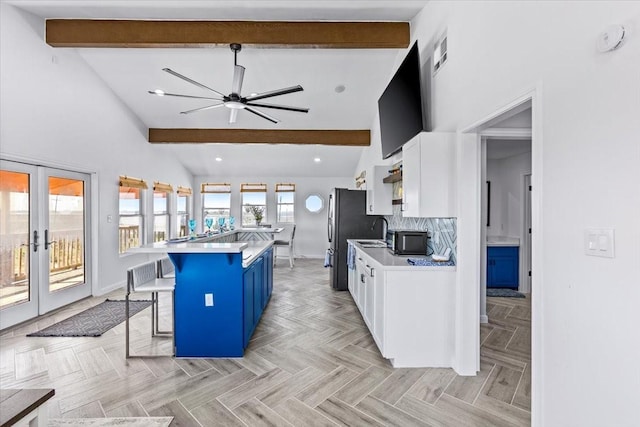 kitchen featuring visible vents, beamed ceiling, a kitchen breakfast bar, freestanding refrigerator, and white cabinets