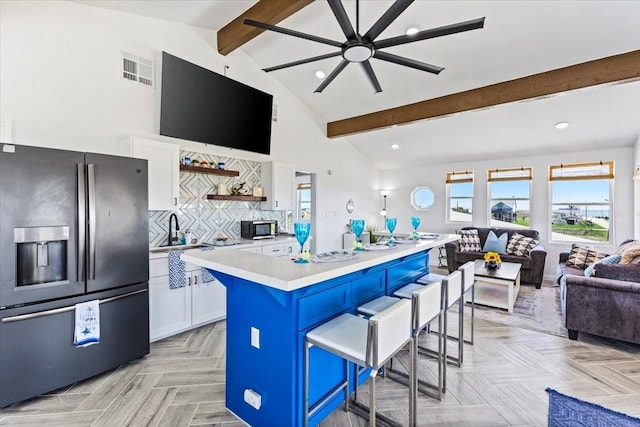 kitchen featuring open floor plan, appliances with stainless steel finishes, a breakfast bar area, white cabinets, and light countertops