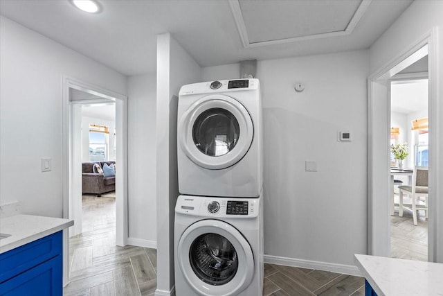 clothes washing area with stacked washer / drying machine, baseboards, and a healthy amount of sunlight