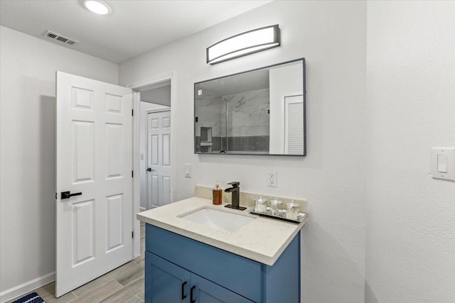 bathroom featuring a marble finish shower, visible vents, baseboards, wood finished floors, and vanity