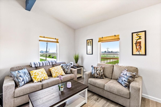 living room featuring vaulted ceiling with beams, baseboards, and wood finished floors