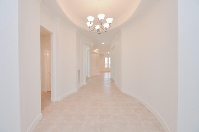 hallway featuring a tray ceiling, a notable chandelier, crown molding, and baseboards