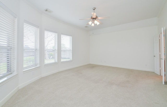 unfurnished room featuring light carpet, a ceiling fan, visible vents, baseboards, and ornamental molding