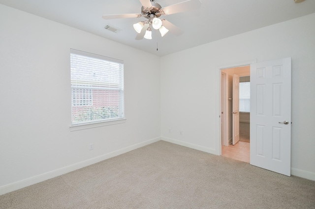 spare room featuring light carpet, a ceiling fan, visible vents, and baseboards