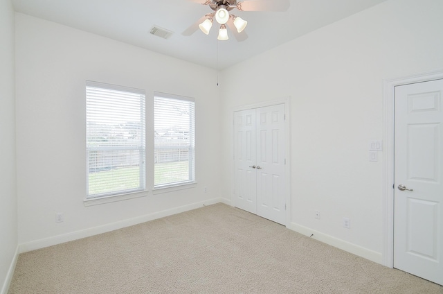 empty room with baseboards, visible vents, ceiling fan, and light colored carpet