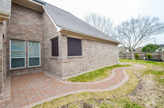 view of side of property with a patio area, a shingled roof, fence, and brick siding