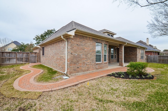 view of home's exterior featuring a patio, a fenced backyard, brick siding, a lawn, and roof with shingles