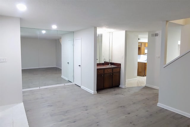 corridor featuring light wood-style flooring, recessed lighting, a sink, visible vents, and baseboards