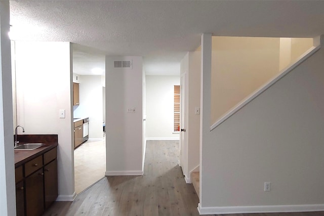 hall featuring a textured ceiling, a sink, visible vents, stairway, and light wood finished floors