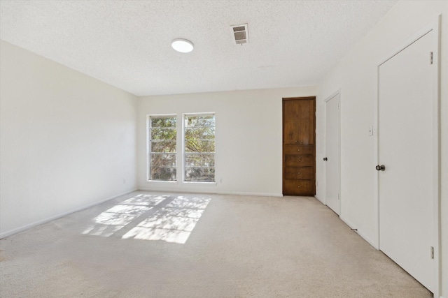 unfurnished bedroom with visible vents, a textured ceiling, and light colored carpet