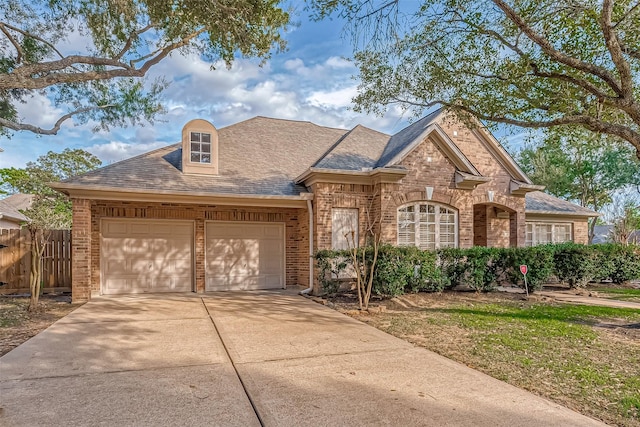 view of front of house with brick siding, a shingled roof, fence, a garage, and driveway