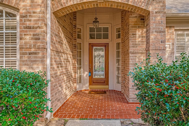 view of exterior entry with roof with shingles and brick siding