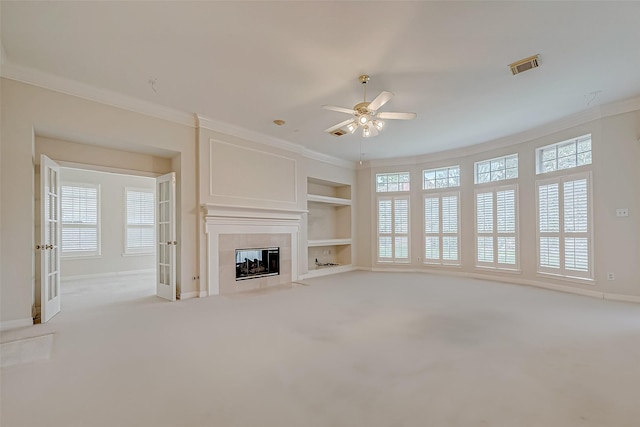 unfurnished living room with visible vents, built in features, a tiled fireplace, light colored carpet, and ornamental molding