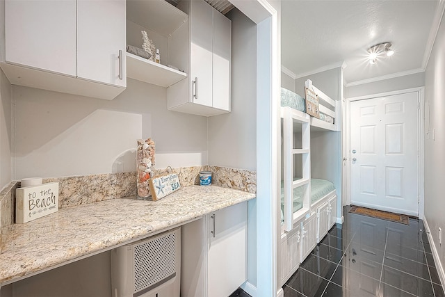 kitchen featuring ornamental molding, white cabinetry, light stone countertops, dark tile patterned floors, and baseboards