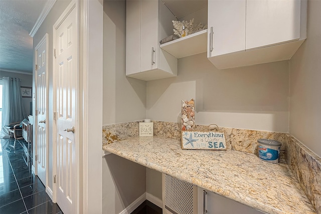 kitchen with light stone counters, dark tile patterned flooring, white cabinets, ornamental molding, and open shelves