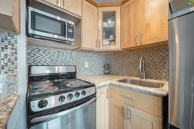 kitchen featuring appliances with stainless steel finishes, glass insert cabinets, a sink, and light stone countertops