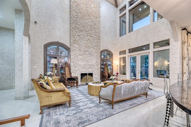 living area with light tile patterned floors, arched walkways, a fireplace, a towering ceiling, and french doors