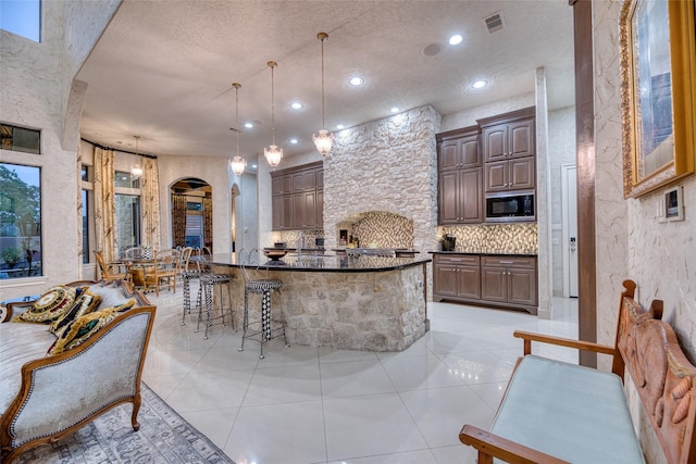 kitchen featuring arched walkways, black microwave, decorative light fixtures, and light tile patterned flooring