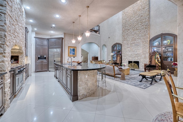 kitchen featuring a center island with sink, arched walkways, premium appliances, open floor plan, and a stone fireplace