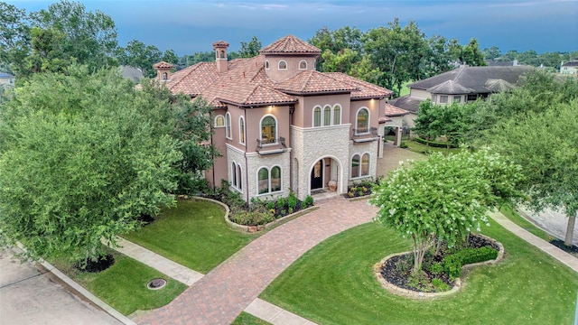 mediterranean / spanish-style house with a balcony, stone siding, a tile roof, a front yard, and stucco siding