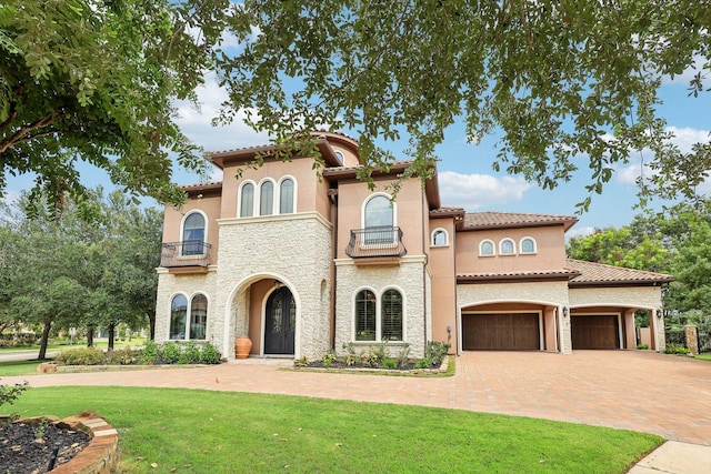 mediterranean / spanish house featuring decorative driveway, a balcony, a front lawn, and stucco siding