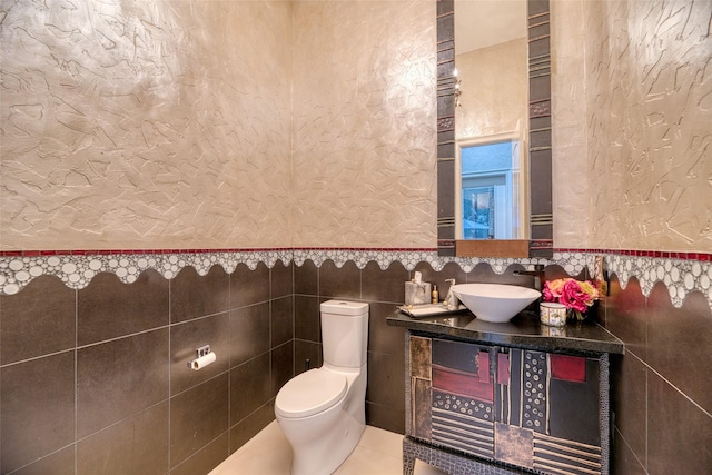 half bathroom featuring tile walls, a textured wall, toilet, vanity, and tile patterned floors