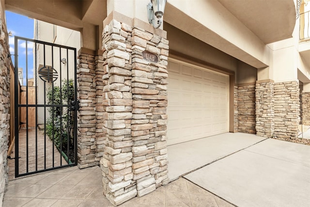 property entrance featuring stone siding, an attached garage, driveway, and stucco siding