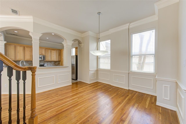 interior space featuring a decorative wall, a sink, visible vents, light wood finished floors, and crown molding