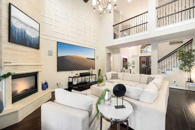 living area with baseboards, dark wood-style floors, a premium fireplace, stairway, and an inviting chandelier