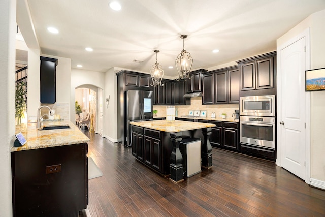 kitchen featuring arched walkways, decorative light fixtures, stainless steel appliances, a sink, and under cabinet range hood