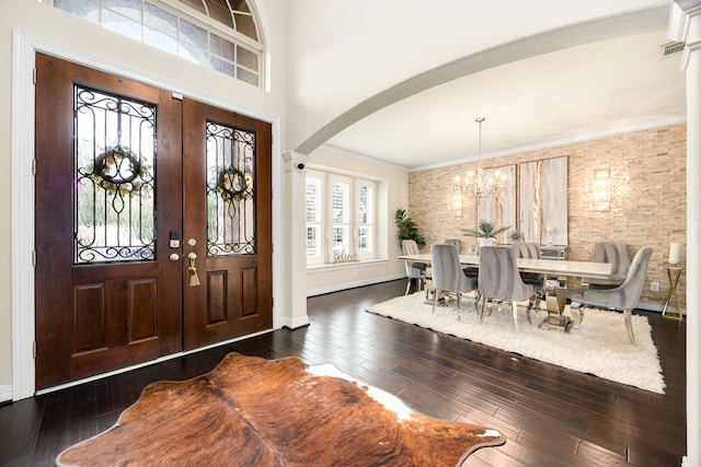 foyer featuring dark wood-style floors, arched walkways, a notable chandelier, and ornamental molding