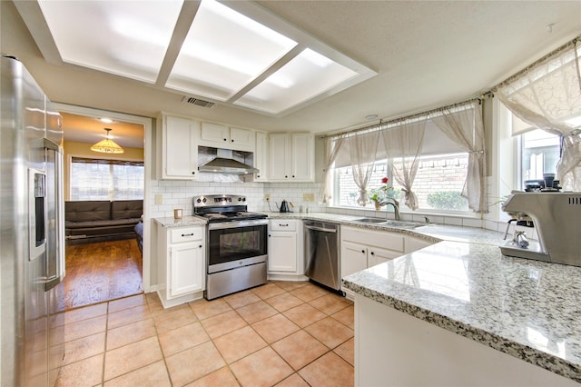 kitchen with pendant lighting, stainless steel appliances, white cabinets, a sink, and wall chimney exhaust hood