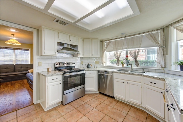 kitchen featuring stainless steel appliances, wall chimney range hood, a sink, and white cabinetry