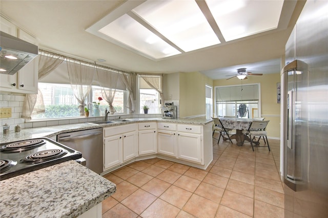 kitchen featuring light tile patterned floors, a peninsula, a sink, white cabinets, and appliances with stainless steel finishes