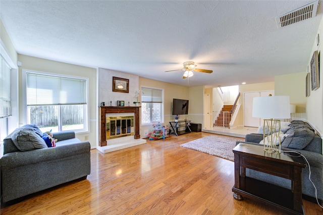 living area with a large fireplace, stairs, visible vents, and light wood-style floors