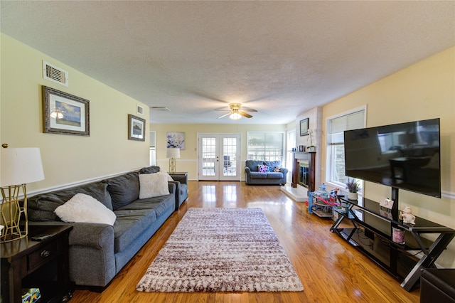 living area featuring visible vents, a glass covered fireplace, wood finished floors, and french doors