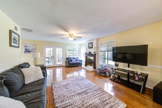 living room featuring french doors, visible vents, a glass covered fireplace, a textured ceiling, and wood finished floors