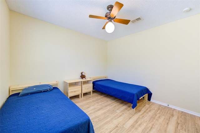 bedroom with light wood-type flooring, ceiling fan, visible vents, and baseboards