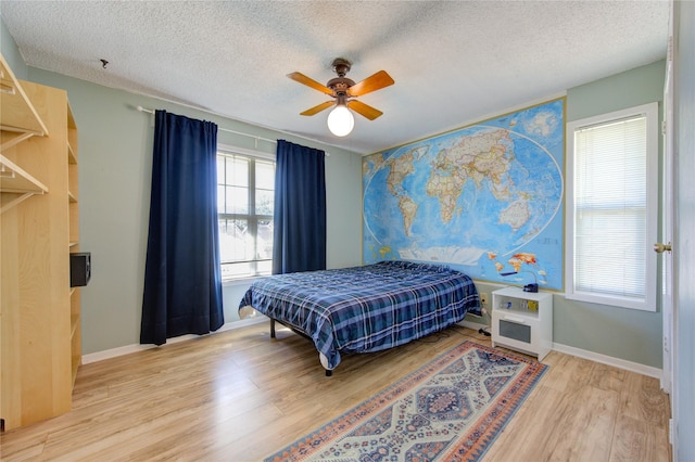 bedroom featuring light wood finished floors, ceiling fan, baseboards, and a textured ceiling