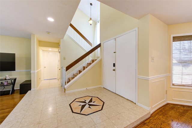 foyer entrance with a wainscoted wall, light tile patterned floors, recessed lighting, a decorative wall, and stairway