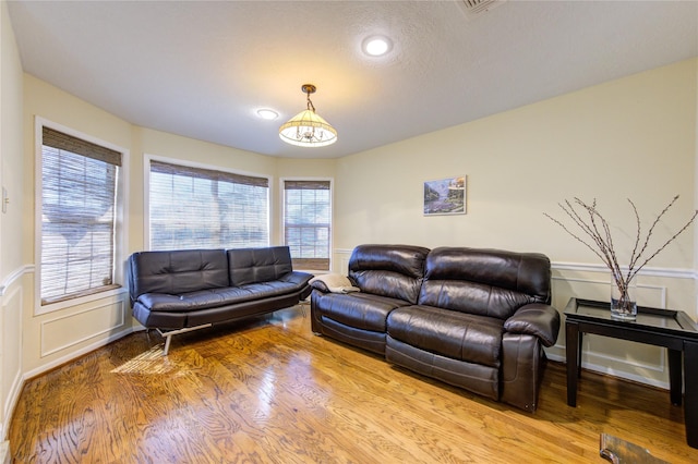 living area featuring light wood-style floors, a chandelier, a decorative wall, and wainscoting