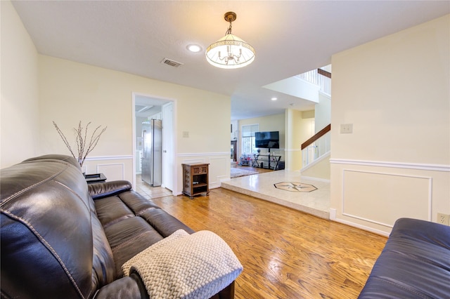 living room featuring light wood-type flooring, a wainscoted wall, visible vents, and stairway