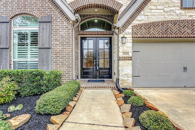 entrance to property featuring french doors, brick siding, concrete driveway, a garage, and stone siding