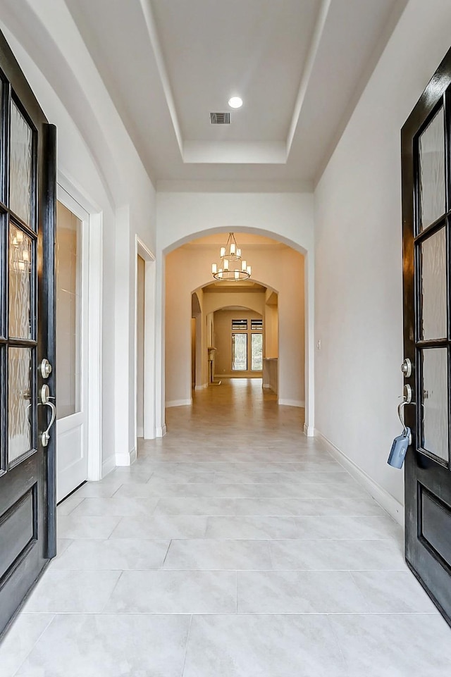 hall with arched walkways, a chandelier, visible vents, baseboards, and a raised ceiling