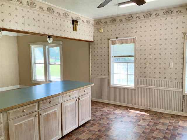 kitchen with wallpapered walls, a ceiling fan, a textured ceiling, and wainscoting