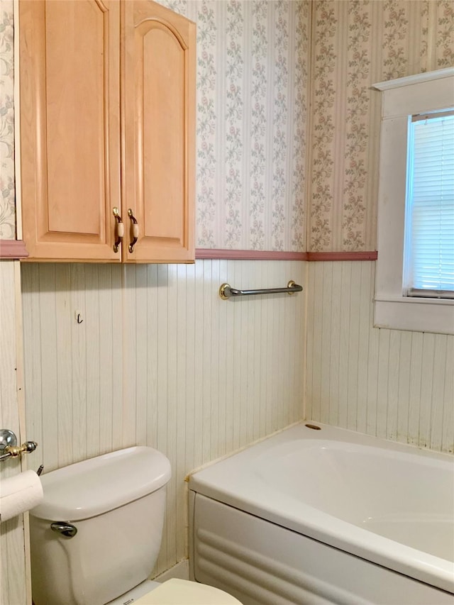 bathroom with a tub, a wainscoted wall, toilet, and wallpapered walls