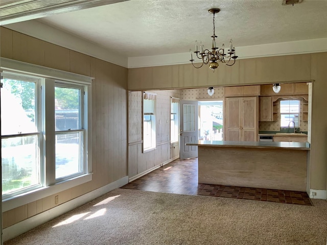 kitchen with carpet, a notable chandelier, light brown cabinetry, a sink, and a textured ceiling