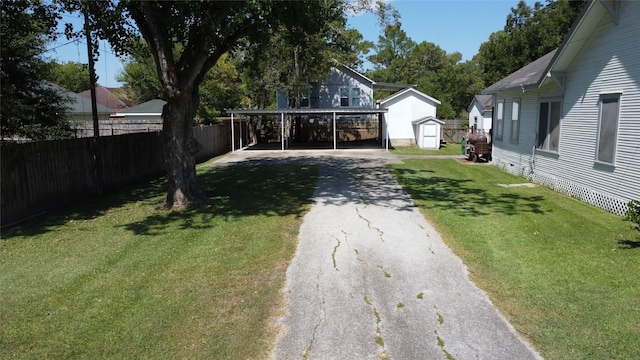 view of yard with an outbuilding, a storage shed, fence, driveway, and a carport