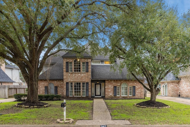 traditional home featuring roof with shingles, brick siding, fence, driveway, and a front lawn