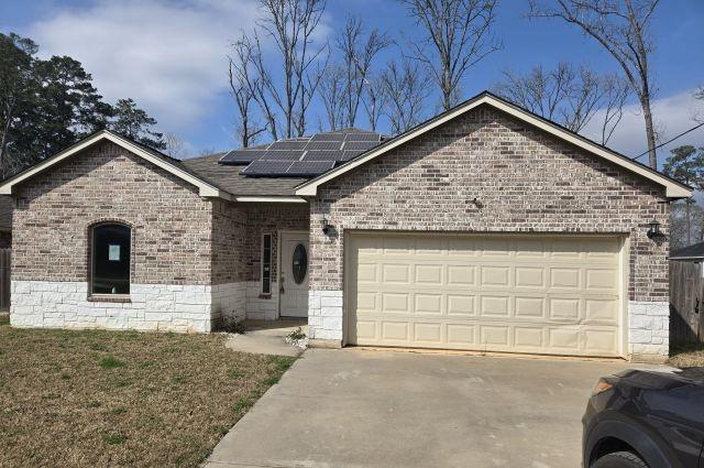 ranch-style house with roof with shingles, brick siding, solar panels, an attached garage, and driveway